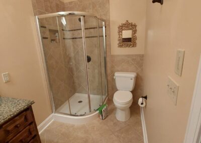 Small bathroom remodel by Bystone in Birmingham, AL, featuring a curved glass corner shower enclosure and neutral tile flooring.